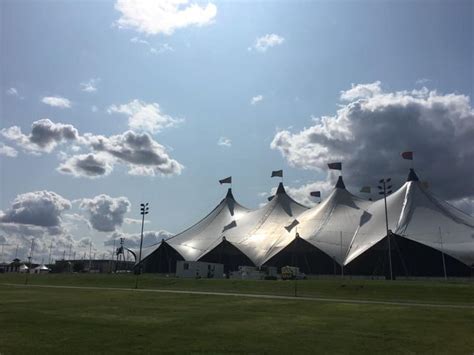 Several Large White Tents Sitting In The Grass Under A Cloudy Blue Sky