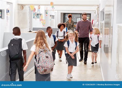 Teacher And Pupils Walking Along Corridor In Busy Elementary School