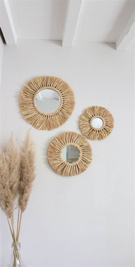 Three Decorative Mirrors On The Wall Above A Vase With Dried Grass In