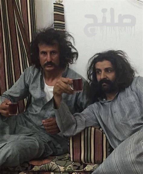 Two Men With Long Hair And Beards Sitting On A Couch Holding Coffee Mugs