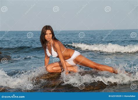 La Bella Giovane Donna Che Si Inginocchia Sulle Rocce Del Mare Porta Il Bikini Immagine Stock