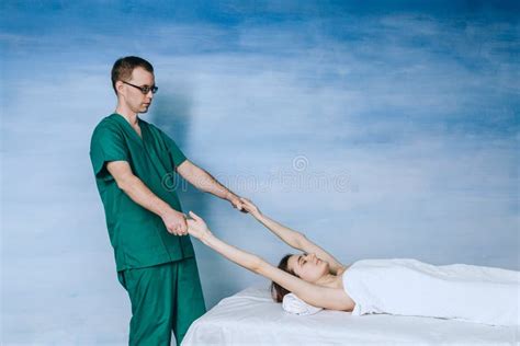 A Man Massage Therapist In Glasses And A Green Uniform Massages The Back Of A Beautiful Woman