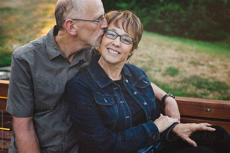 Middle Aged Retired Couple Kissing And Cuddling Outside Sitting On A