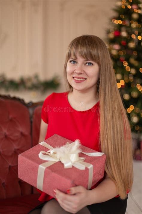 Portrait Of A Beautiful Blonde Girl With A Christmas Gift Near The Christmas Tree Stock Photo