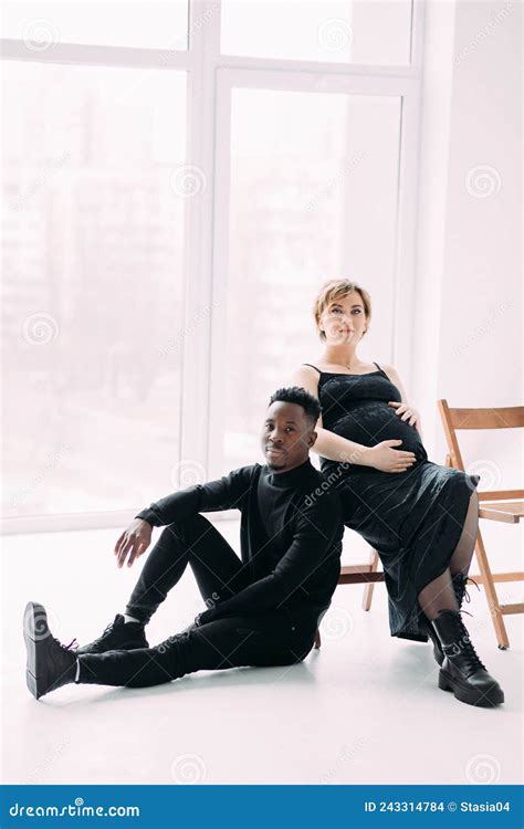 Young African Man And His Caucasian Pregnant Woman Sit On Chairs Stock