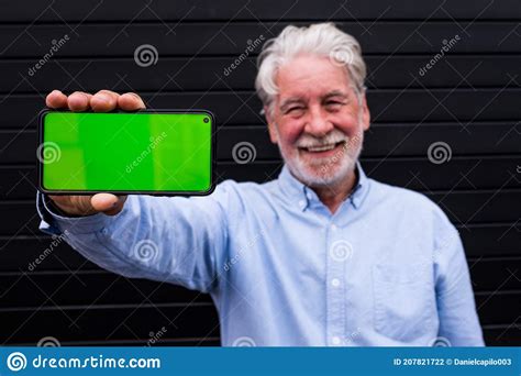 Old And Mature Man Holding His Smartphone Showing It At The Camera With