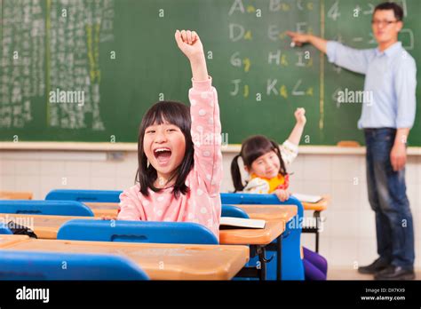 Happy Pupils Raising Hands During The Lesson In The Classroom Stock