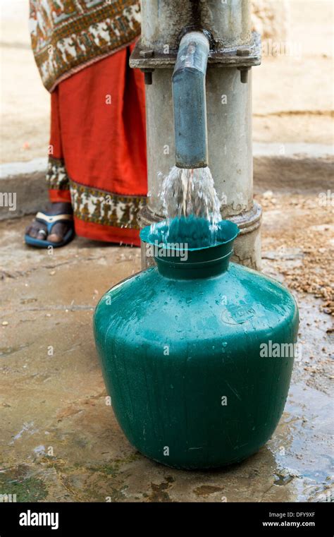 Rural Indian Woman Filling Plastic Water Pot From A Rural Water Pump