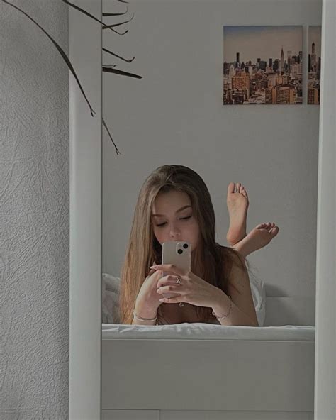 A Woman Taking A Selfie With Her Cell Phone In The Mirror While Sitting