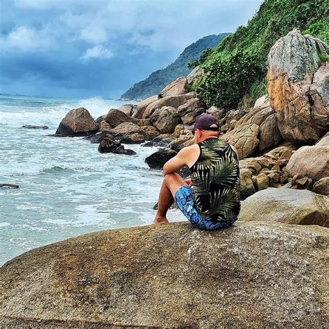 A Man Sitting On Top Of A Large Rock Next To The Ocean