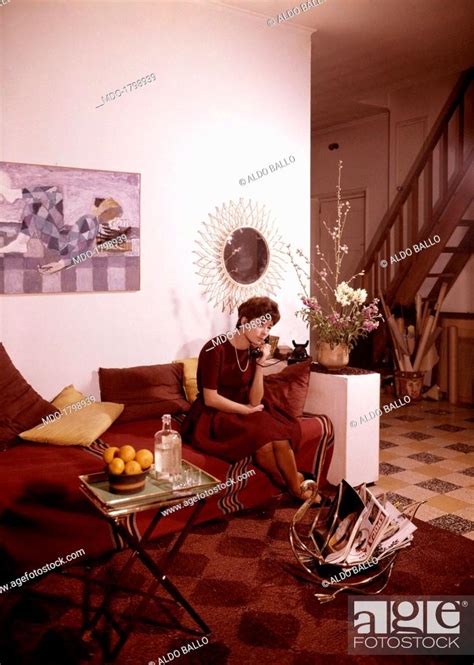 A woman speaking over the telephone sitting on a sofa in a living room ...