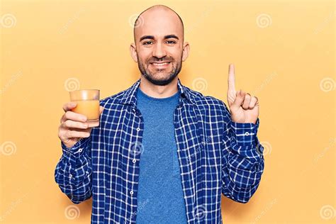 Young Handsome Bald Man Drinking Glass Of Healthy Orange Juice Smiling