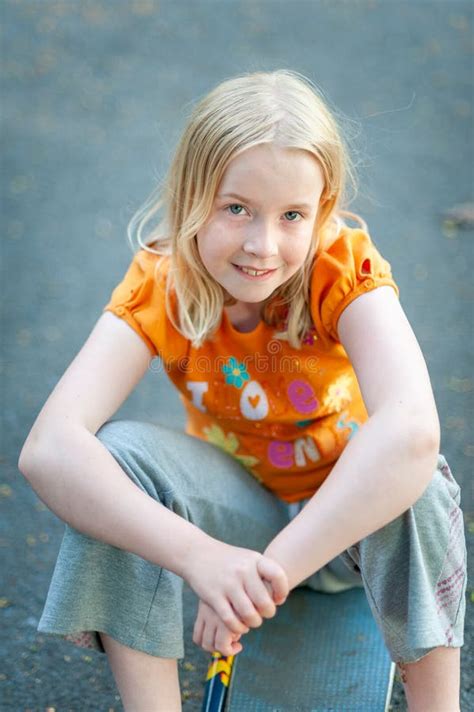 Happy Pretty Blonde Girl Smiling And Sitting On A Skateboard While Making Eye Contact Stock