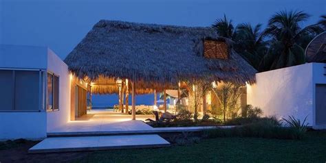 A Thatched Roof House With Lights On At Night