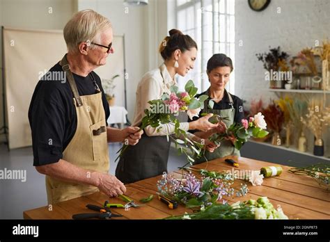 Portrait Of Smiling Female Florist Teaching Mature Couple Arranging