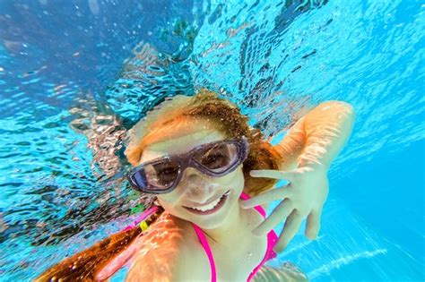 Niña sonriente en gafas de natación nadando bajo el agua en la piscina