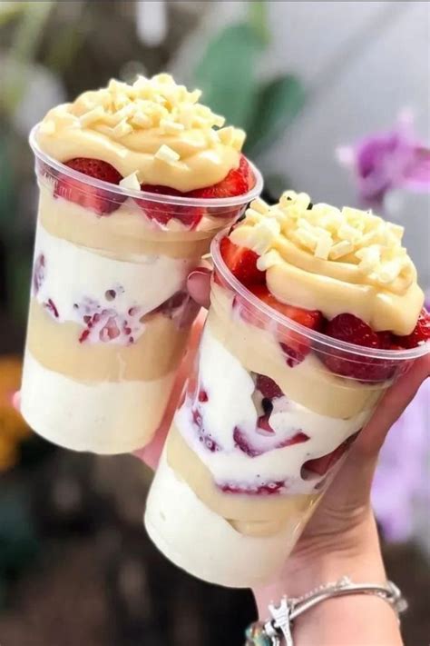 Two Dessert Cups With Strawberries And Whipped Cream On Top Are Being