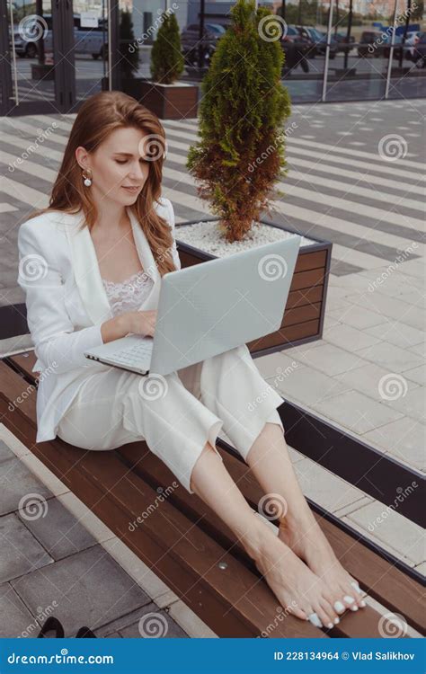 Barefoot Businesswoman In White Suit Sitting On Bench With Laptop