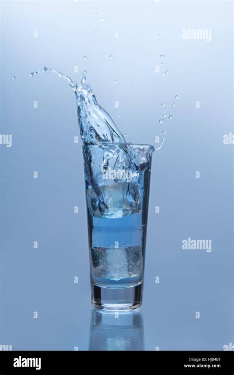 An Ice Cube Falling Into Glass Of Water On Blue Background Stock Photo