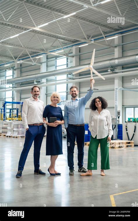 Mature Businessman Holding Wind Turbine Model Standing By Colleagues In