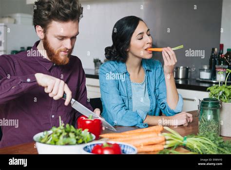 Young Man Chopping Red Bell Pepper Beside Woman Eating Carrot At