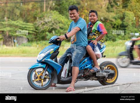 A Thai father and son, sat on a modified, custom motor scooter with extended swing arm and gold ...