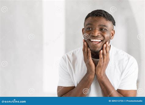 Young African American Man Smiles Happily Touching Face In Bathroom