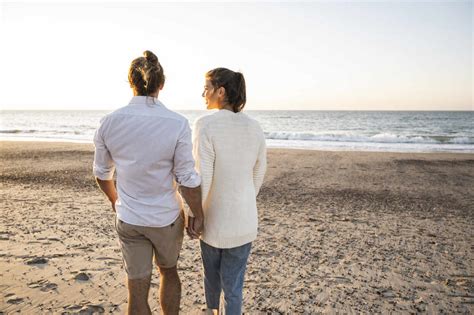 Junges Paar Hält Hände Beim Spaziergang Am Strand Bei Sonnenuntergang Lizenzfreies Stockfoto