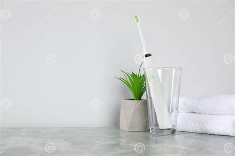 Electric Toothbrush In Glass Towels And Green Houseplant On Light Grey