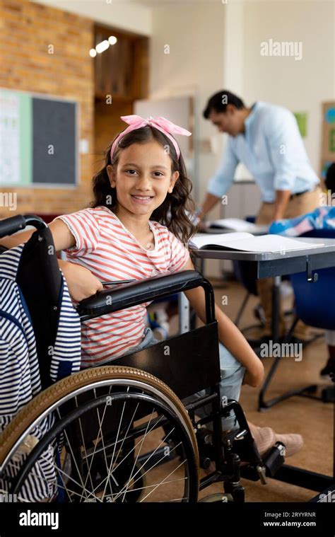 Portrait Of Happy Biracial Girl In Wheelchair In Class At Elementary