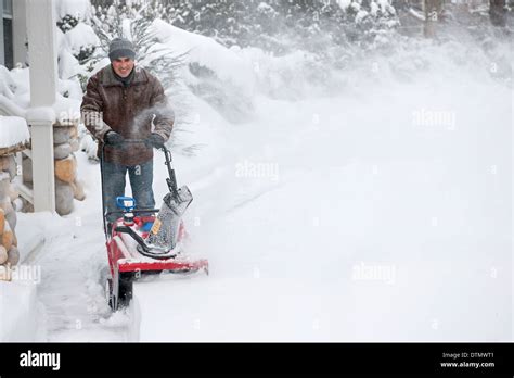 Man Using Snowblower To Clear Deep Snow On Driveway Near Residential