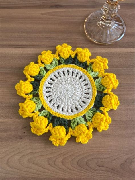 A Crocheted Doily With Yellow Flowers On A Wooden Table Next To A Wine