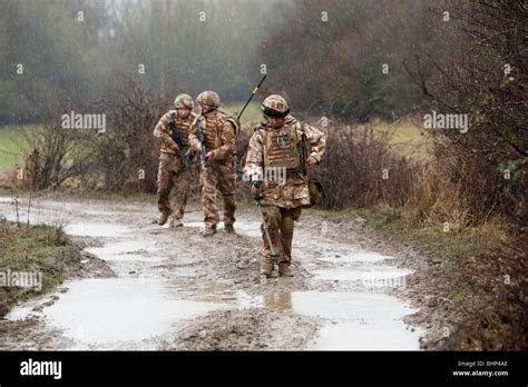 Three British Soldier Walking In Line Along A Muddy Road Behind A Metal