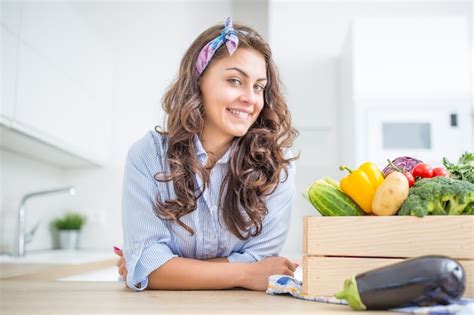 Mujer en su cocina con caja de madera llena de vegetales orgánicos