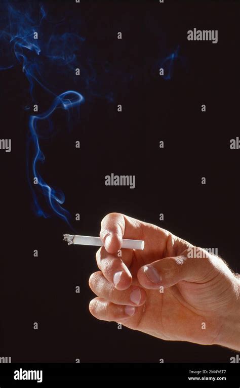 Close Up Shot Of A Hand Holding A Cigarette Smoke Is Billowing Away