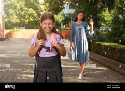 Mother Waving Goodbye To Her Daughter Before School Outdoors Stock