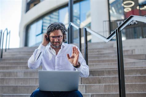 Portrait Of Mature Businessman Sitting On Stairs In City Working On