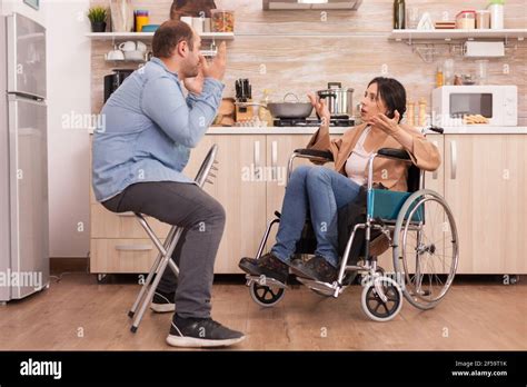 Disabled wife in wheelchair shouting at husband in kitchen. Disabled ... 