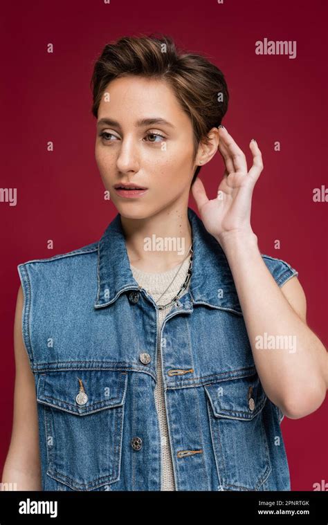 Stylish Model In Denim Outfit With Vest Fixing Her Short Hair On Burgundy Background Stock Image