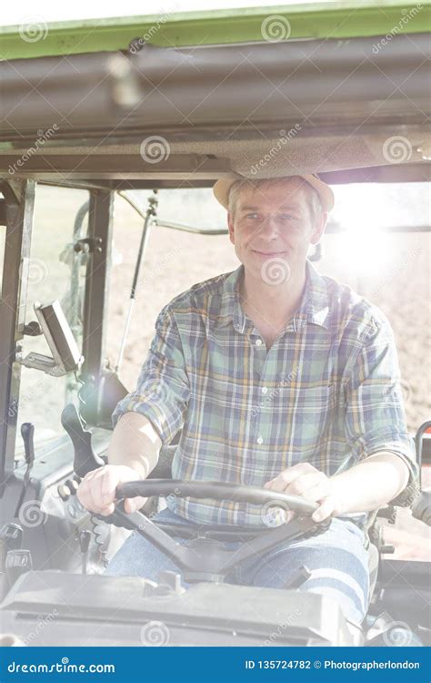 Smiling Confident Mature Farmer Driving Tractor At Farm Stock Photo