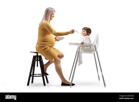 Pregnant Woman Feeding A Baby In A Chair Isolated On White Background