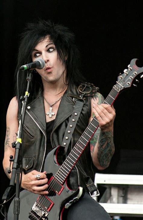 A Man With Black Hair And Piercings Holding A Guitar In Front Of A