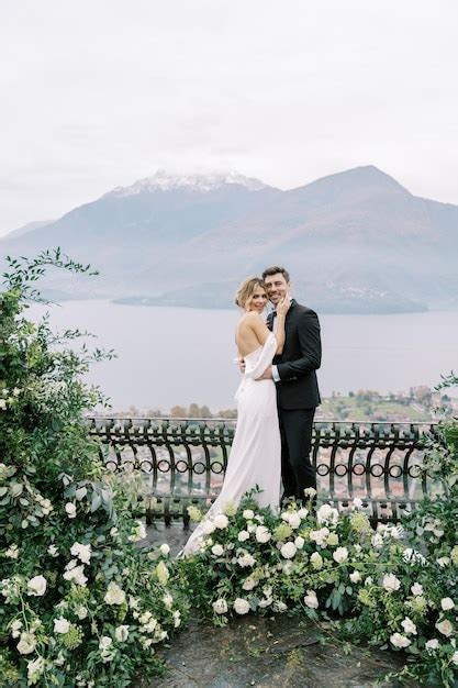 Premium Photo Smiling Groom Hugs His Bride Waist Near A Fence With