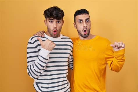 Jeune Couple Gay Hispanique Debout Sur Fond Jaune Surpris Pointant Main Sur Le Côté Ouvert