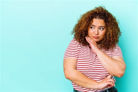 Joven mujer curvilínea latina aislada sobre fondo azul mirando hacia los lados con expresión