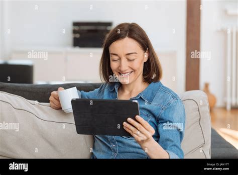 Mature Woman Using Tablet Computer While Relaxing On Sofa At Home Stock