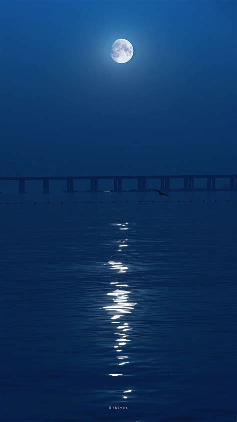 The Full Moon Is Shining Over The Water And Bridge In The Distance With