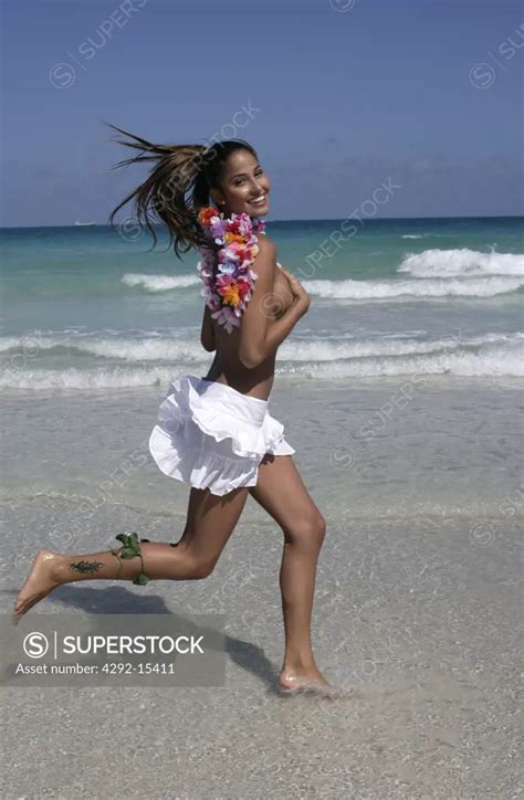 Young Woman Running On A Sunny Beach Wearing A White Skirt And Leis