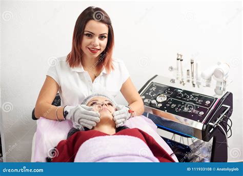 Woman Cosmetologist Is Giving Facial Massage To A Female Patient In A