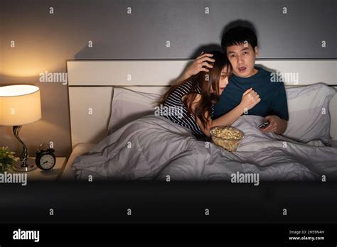 Scared Young Couple Is Watching Horror Movie Tv On A Bed At Night Stock